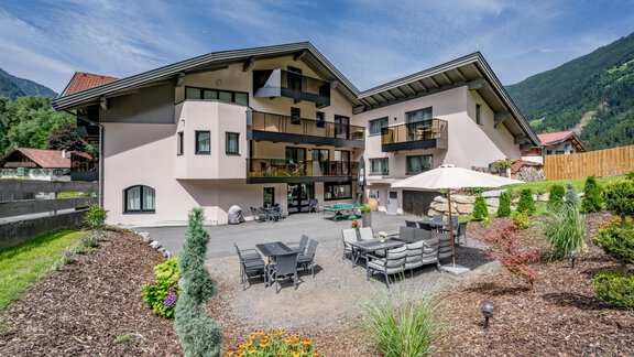 Ein modernes Gebäude mit mehreren Balkonen und einer einladenden Terrasse. Der Garten ist mit bunten Blumen und grünen Pflanzen gestaltet. - Appartements Perberschlager - Oetz