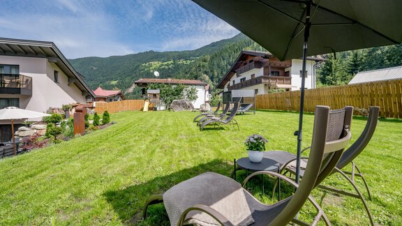 A well-maintained garden with loungers and parasols. In the background, several chalets and mountains can be seen. - Appartements Perberschlager - Oetz