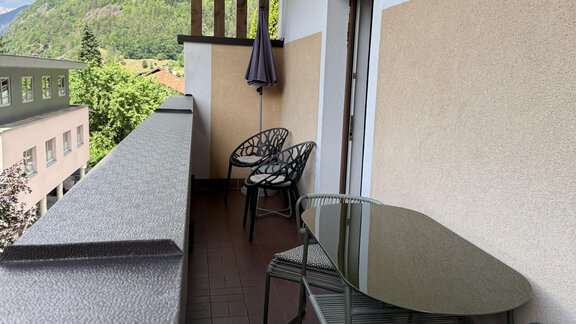 A balcony with a table and chairs. In the background, green mountains and a blue sky can be seen. - Appartements Schmid Peter - Oetz