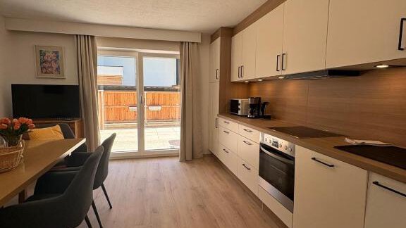A modern kitchen with a large window and access to a terrace. The room is bright and friendly, furnished with a dining area and modern appliances. - Haus Evi - Oetz