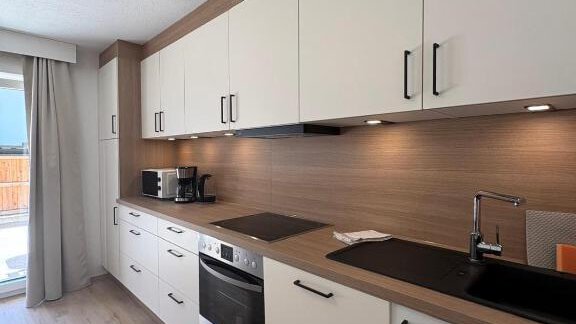A modern kitchen with white cabinets and wooden details.  
It is well equipped with appliances and has plenty of natural light. - Haus Evi - Oetz
