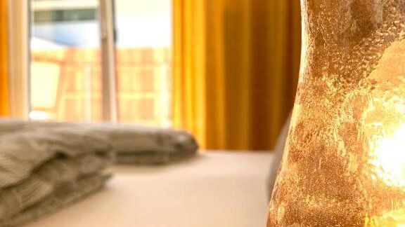 A cozy room with warm yellow curtains and a view of a balcony. On a table, there is a decorative, glowing candle. - Haus Evi - Oetz