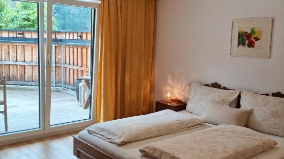 Cozy bedroom with a double bed and a large window front. A warm color tone of the curtains and a decorative picture create an inviting atmosphere. - Haus Evi - Oetz