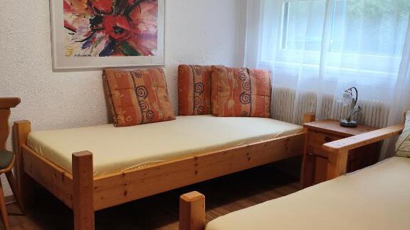 A simple bedroom with two single wooden beds.  
A colorful painting hangs on the wall, and the room has large windows with daylight. - Haus Evi - Oetz