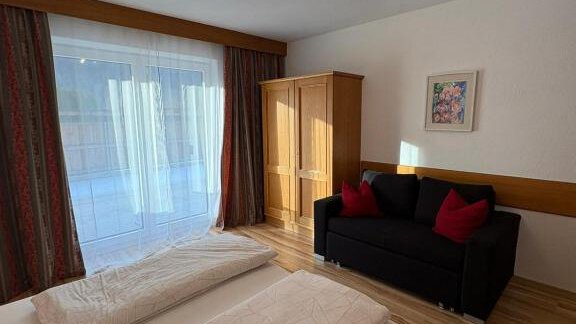 A bright room with two single beds and a black sofa.  
Large windows let in plenty of daylight. - Haus Evi - Oetz
