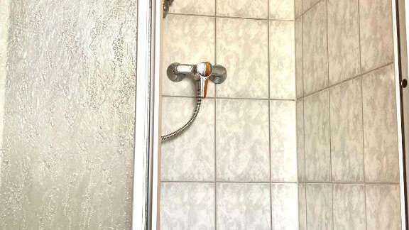 A shower with white tiles and a showerhead. On the floor, there is a bottle of shower gel. - Haus Evi - Oetz