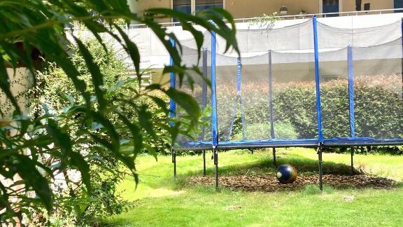 A garden with a trampoline and green grass. In the background, some plants and a building are visible. - Haus Evi - Oetz