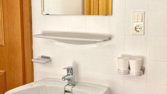 A modern bathroom with a sink and a large mirror. Next to the sink are towels and two cups. - Haus Evi - Oetz