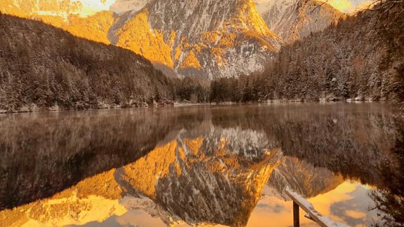 A picturesque lake surrounded by majestic mountains. The golden reflections in the water create a peaceful atmosphere. - Haus Evi - Oetz