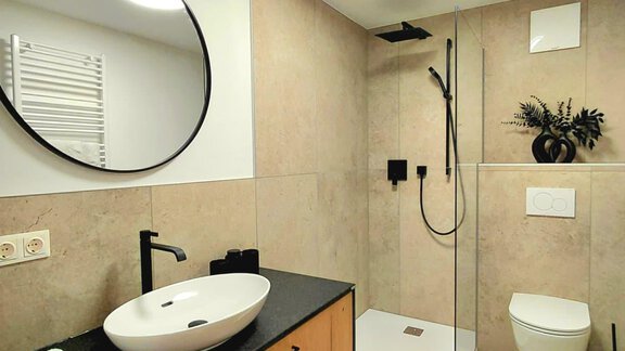 A modern bathroom with an elegant shower and a simple sink. The walls are in neutral tones, and there is a large mirror. - Haus Gstrein - Oetz