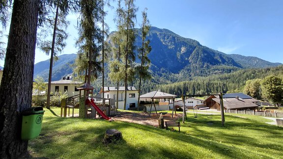 A playground surrounded by trees and with a view of majestic mountains. The sky is clear and the landscape is green and inviting. - Haus Gstrein - Oetz
