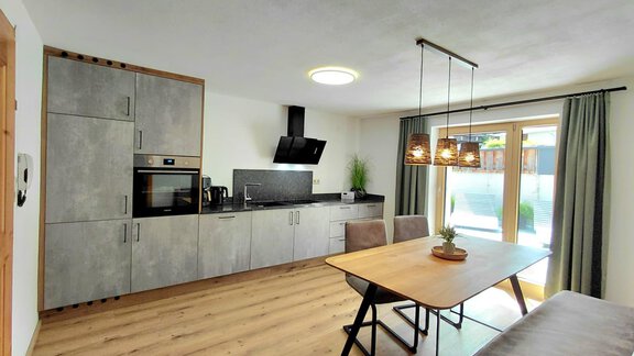 A modern kitchen with gray furniture and a dining area. The light comes through large windows that offer a view outside. - Haus Gstrein - Oetz
