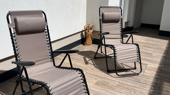 Zwei relaxende Liegen stehen auf einer sonnigen Terrasse. Die Oberfläche ist mit Holzfliesen gestaltet, und eine dekorative Figur ist im Hintergrund sichtbar. - Haus Juen - Oetz