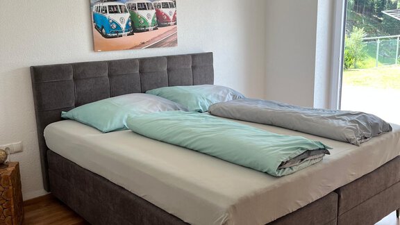 Ein modernes Schlafzimmer mit einem großen Bett und hellen Bettdecken. Das Zimmer hat ein Fenster mit Blick ins Freie und ein farbenfrohes Bild an der Wand. - Haus Juen - Oetz