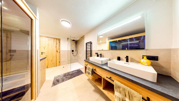 Ein modernes Badezimmer mit zwei Waschbecken und eleganten Armaturen. Die helle Ausstattung und die Holzdetails schaffen eine einladende Atmosphäre. - Haus Matteo - Oetz