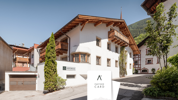 Ein charmantes Gebäude im alpinen Stil mit einem klaren blauen Himmel. Im Vordergrund sind Partnerkarten zu sehen. - MYALPS Historical - Oetz