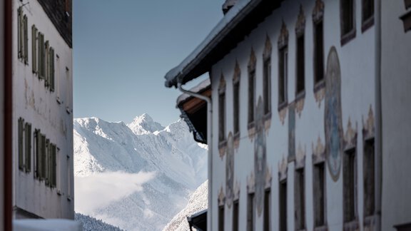 Eine winterliche Landschaft mit schneebedeckten Bergen im Hintergrund. Im Vordergrund sind zwei traditionelle Gebäude zu sehen. - MYALPS Historical - Oetz
