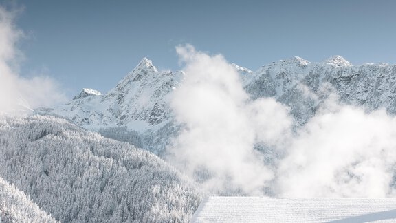 Eine schneebedeckte Berglandschaft mit hohen Gipfeln und einem klaren Himmel. Nebel umhüllt einige Bereiche der Berge, was eine ruhige Atmosphäre schafft. - MYALPS Historical - Oetz
