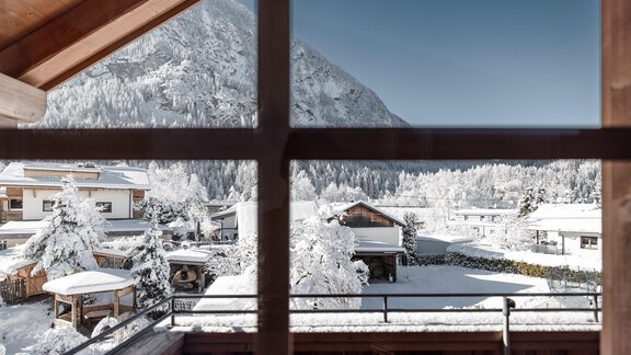 Eine winterliche Landschaft mit schneebedeckten Dächern und Bäumen. Im Hintergrund sind Berge unter klarem Himmel zu sehen. - MYALPS Mühlhof - Oetz