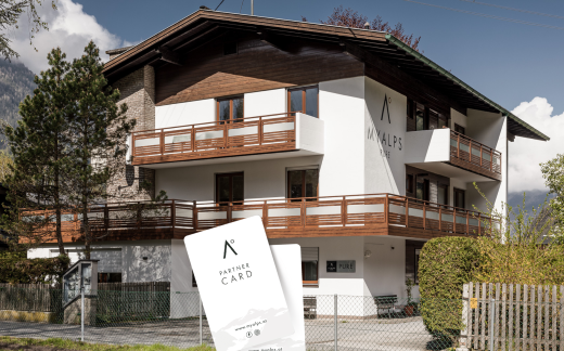 A modern building with several balconies and a beautiful fence. In the foreground is a partner card promoting the offerings of the house. - MYALPS Pure - Oetz