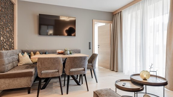 Ein modernes Wohnzimmer mit einem großen Tisch und gepolsterten Stühlen. Große Fenster sorgen für viel Tageslicht und eine gemütliche Atmosphäre. - MYALPS Tirol - Oetz