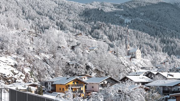 Eine verschneite Berglandschaft mit hübschen Häusern und einer Kirche. Die Bäume und der Boden sind vollständig mit Schnee bedeckt. - MYALPS Tirol - Oetz
