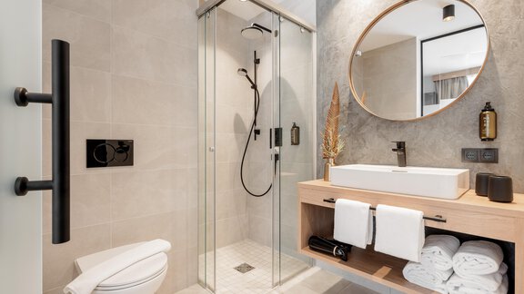 Ein modernes Badezimmer mit einer gläsernen Dusche und einem großen Spiegel. Die Holzkommode hat Handtücher ordentlich gestapelt. - MYALPS Tirol - Oetz