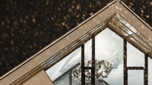 Ein modernes Dachfenster mit einer künstlerischen Lampe im Inneren. Draußen fällt Schnee, während die Lichter warm strahlen. - MYALPS Tirol - Oetz