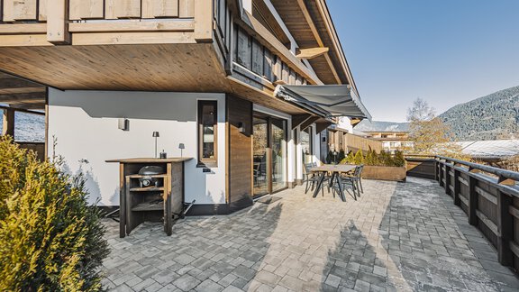Eine moderne Terrasse mit einem Grill und Sitzgelegenheiten. Im Hintergrund sind Berge und ein klarer Himmel zu sehen. - See das Ferienhaus - Oetz