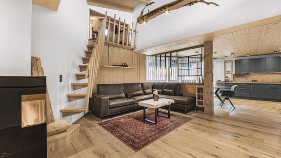 Ein modernes Wohnzimmer mit einer bequemen Couch und einem Tisch. Eine Holztreppe führt in den oberen Bereich des Raumes. - See das Ferienhaus - Oetz