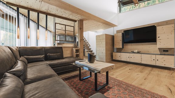 Ein modernes Wohnzimmer mit einem großen, beigen Sofa und einem stilvollen Couchtisch. Holzelemente und große Fenster sorgen für ein helles und einladendes Ambiente. - See das Ferienhaus - Oetz