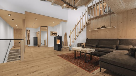 Ein modernes Wohnzimmer mit einem komfortablen Sofa und einem holzverkleideten Treppenbereich. Der Raum hat einen warmen Holzfußboden und eine gemütliche Atmosphäre. - See das Ferienhaus - Oetz