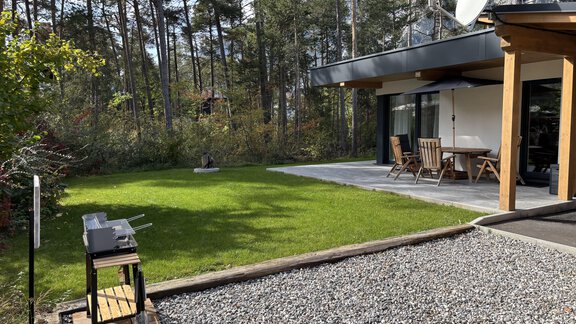A modern house with a terrace and a well-kept green lawn. In the foreground, there is a grill on a wooden stand. - Residenz Bergzauber - Ötztal Bahnhof