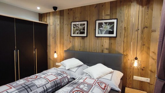 A cozy bedroom with two beds and wooden paneling. Pictures hang on the wall, and there is soft lighting. - Alpenchalet Valentin - Sautens