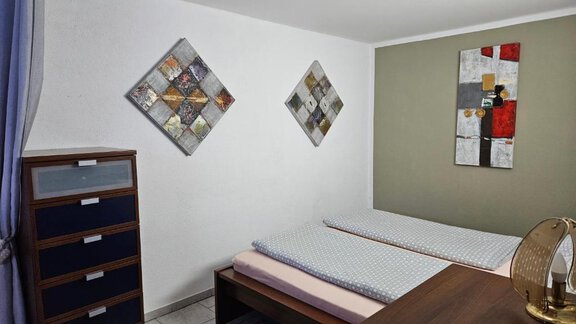 The room is simply and modernly furnished, with a bed, a nightstand, and a dresser. Decorative pictures in neutral colors hang on the walls. - Appartement Harmony - Sautens