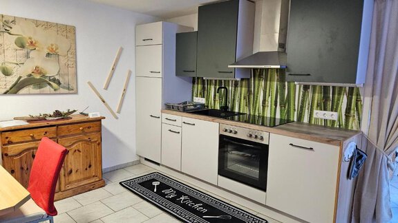 A modern kitchen with white and black cabinets.  
There is a carpet on the floor and green bamboo patterns on the wall. - Appartement Harmony - Sautens
