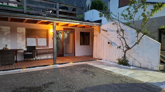 An inviting entrance to a modern house. The facade is brightly lit and there is a small table with chairs on the terrace. - Appartement Harmony - Sautens