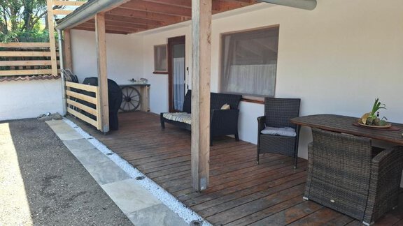An inviting porch with a wooden floor and cozy furniture. In the background, a door and a grill can be seen. - Appartement Harmony - Sautens