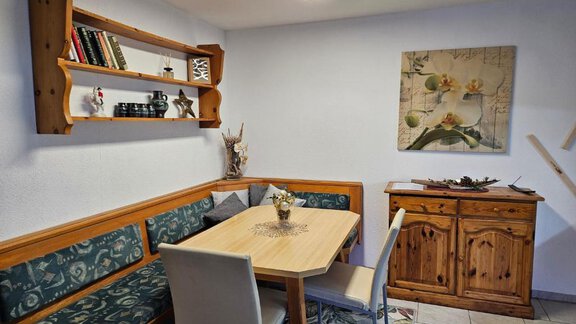 A cozy dining area with a wooden bench and a table. On the wall is a picture with floral motifs and a shelf with books. - Appartement Harmony - Sautens