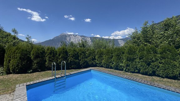 Ein klarer, blauer Pool mit einer Leiter und üppigem Grün rundherum. Im Hintergrund sind majestätische Berge und ein strahlend blauer Himmel zu sehen. - bei Herrmann´s - Sautens