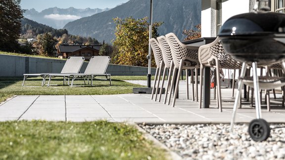 Eine moderne Terrasse mit einem Essbereich und Liegen. Im Hintergrund sind Berge und ein blauer Himmel zu sehen. - Chalet Pirchhof by MYALPS - Sautens