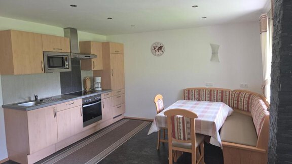 A modern kitchen with wooden cabinets and a dining table. The room is bright and inviting. - Ferienhof Strigl - Sautens