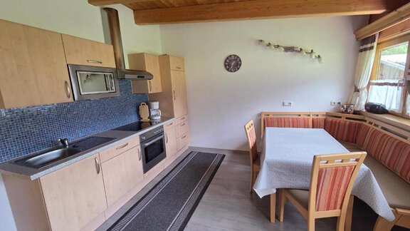 Modern kitchen with wooden ceiling and open dining area.  
Bright colors and cozy furnishings create an inviting atmosphere. - Ferienhof Strigl - Sautens
