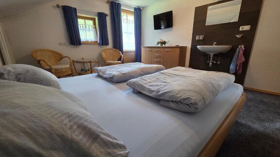 A cozy bedroom with a large bed, two pillows, and a modern sink. There are two chairs and a television on the wall. - Ferienhof Strigl - Sautens