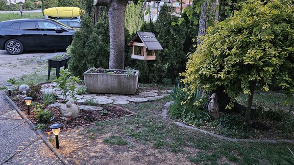 Ein hübscher Garten mit einer kleinen Sitzecke und einem Brunnen. Im Hintergrund sind Bäume und ein Parkplatz sichtbar. - Ferienwohnungen Inka - Sautens