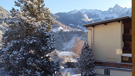 Eine verschneite Landschaft mit hohen Bergen im Hintergrund. Im Vordergrund sind Bäume und ein schneebedeckter Weg zu sehen. - Oxy Holiday - Sautens