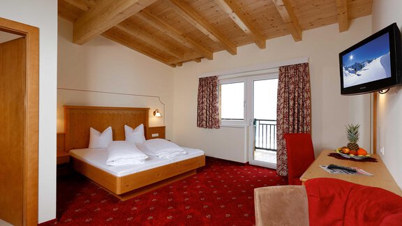 A cozy hotel room with a wooden ceiling and a red carpet. It is decorated with a double bed, a television, and a small table. - Alp Resort Tiroler Adler - Sölden