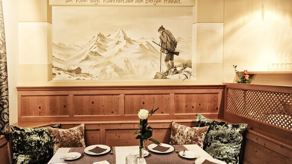 A cozy dining room with traditional wooden furniture and a beautiful mountain painting in the background. The table is elegantly set with a floral decoration. - Alp Resort Tiroler Adler - Sölden