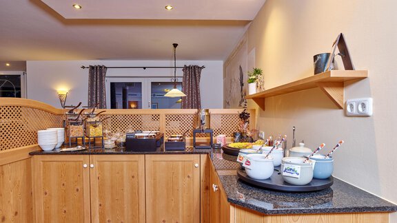 A modern kitchen corner with wooden cabinets and a granite countertop. Various breakfast options and utensils are on the counter. - Alp Resort Tiroler Adler - Sölden