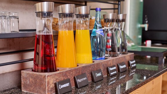 A selection of drinks in glass carafes is on a table. The colors range from red to orange to clear water. - Alp Resort Tiroler Adler - Sölden